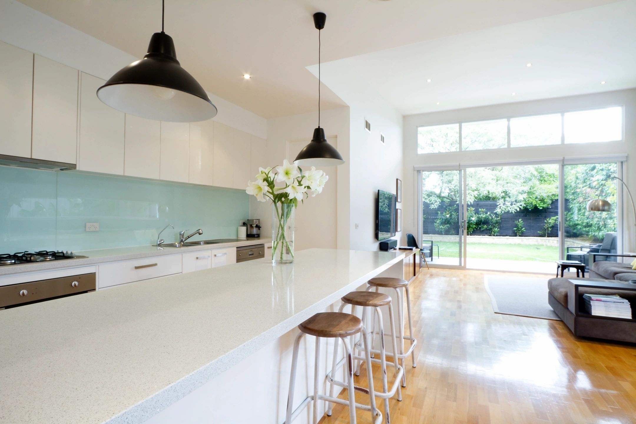 A kitchen with white counters and black pendants.