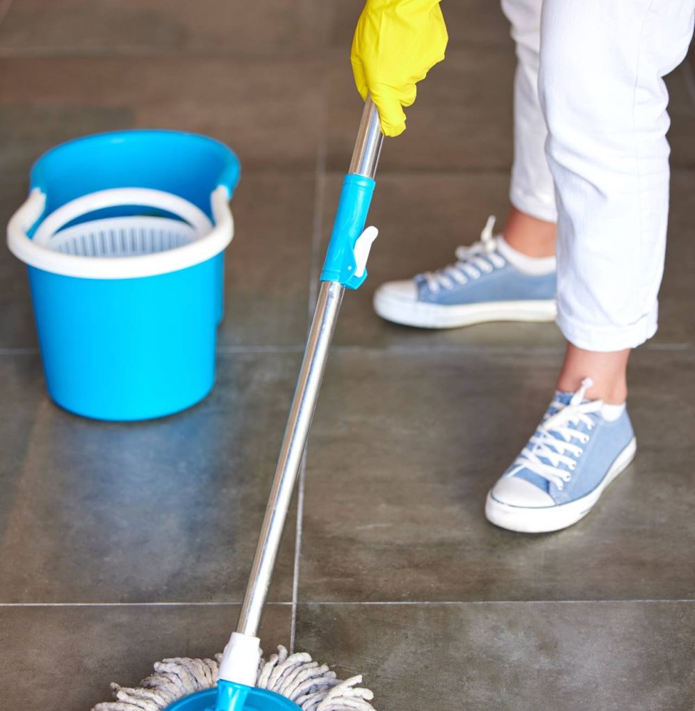 A person wearing yellow and white cleaning the floor